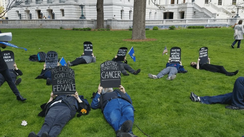 protestors lay in the grass with tombstone signs