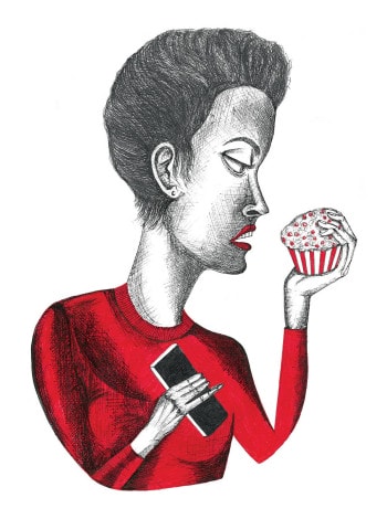 A woman holding a cupcake stares into its sprinkled frosting, ignoring the phone she holds in her other hand.