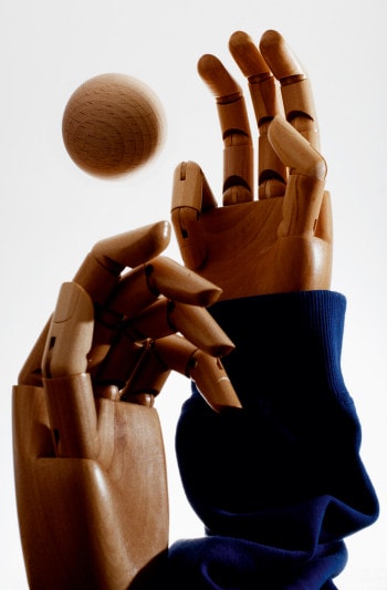 Two wooden hands reach up for a wooden ball.